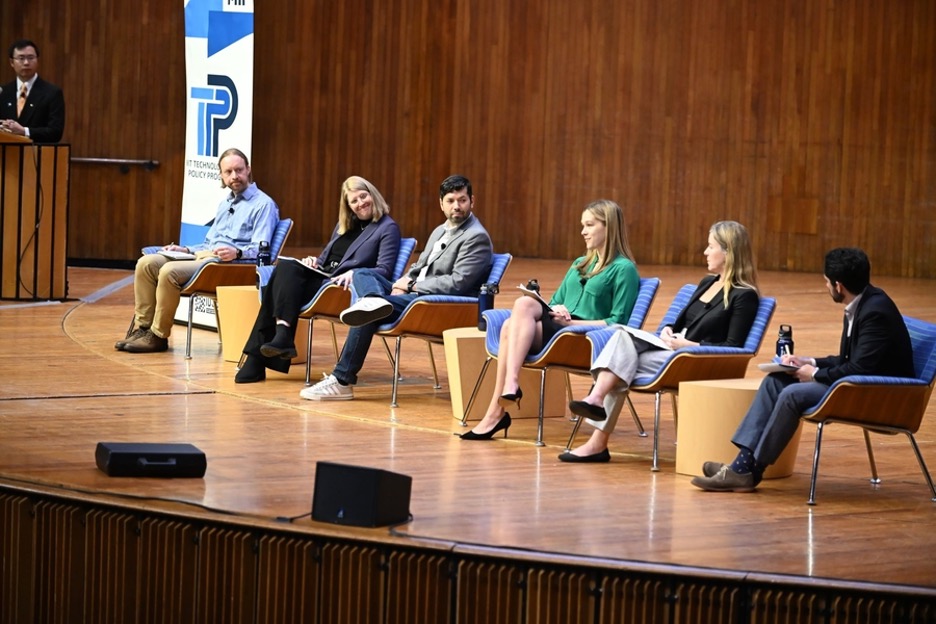 Image of 6 panelists sitting on stage while one speaks.
