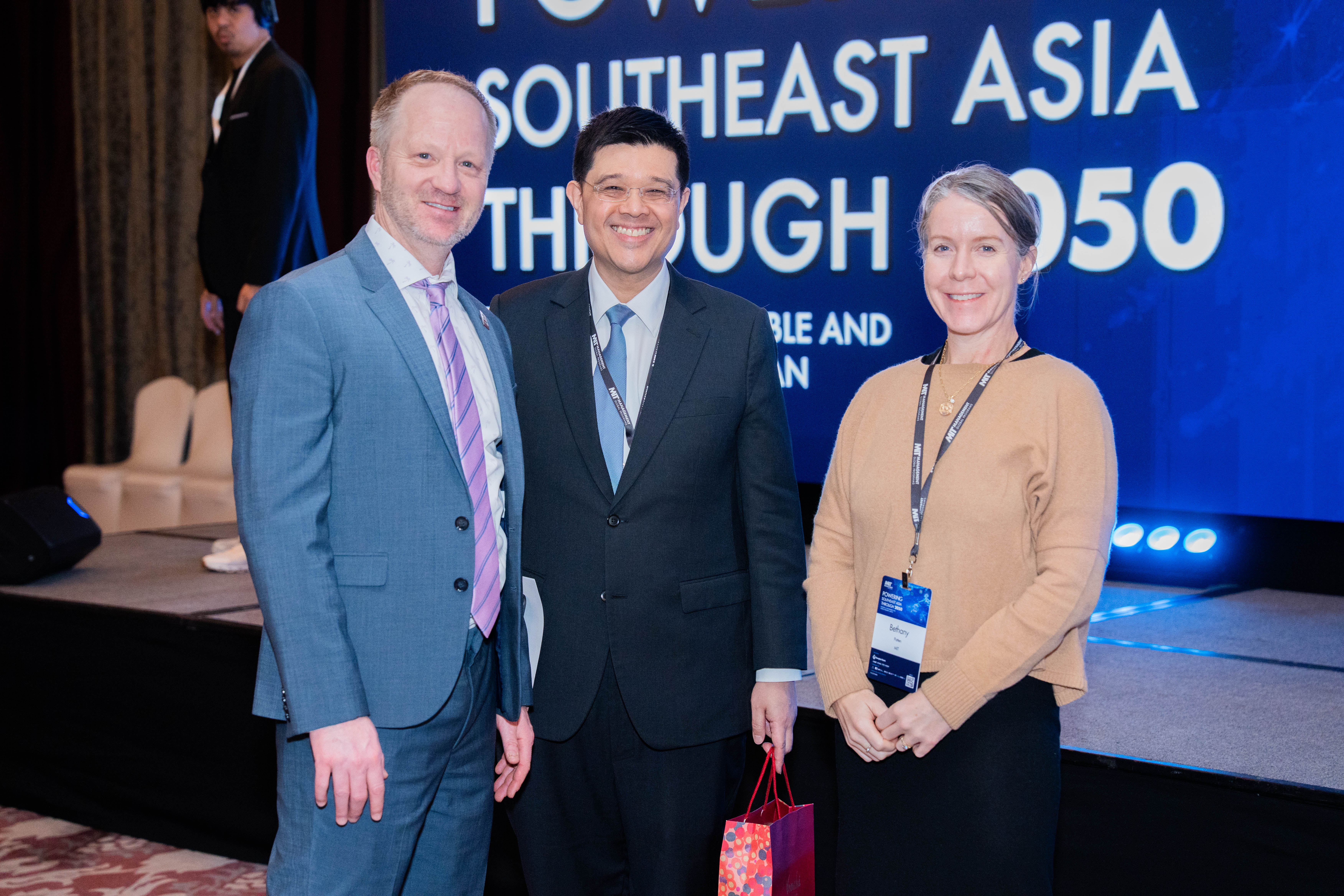 Three people smile and pose for a picture in front of a stage