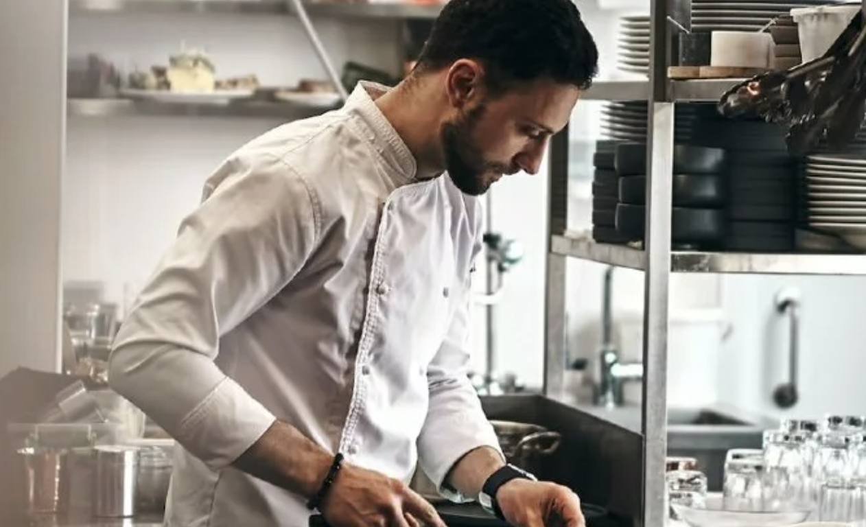 Man in a white chef's coat cutting something in an industrial kitchen 