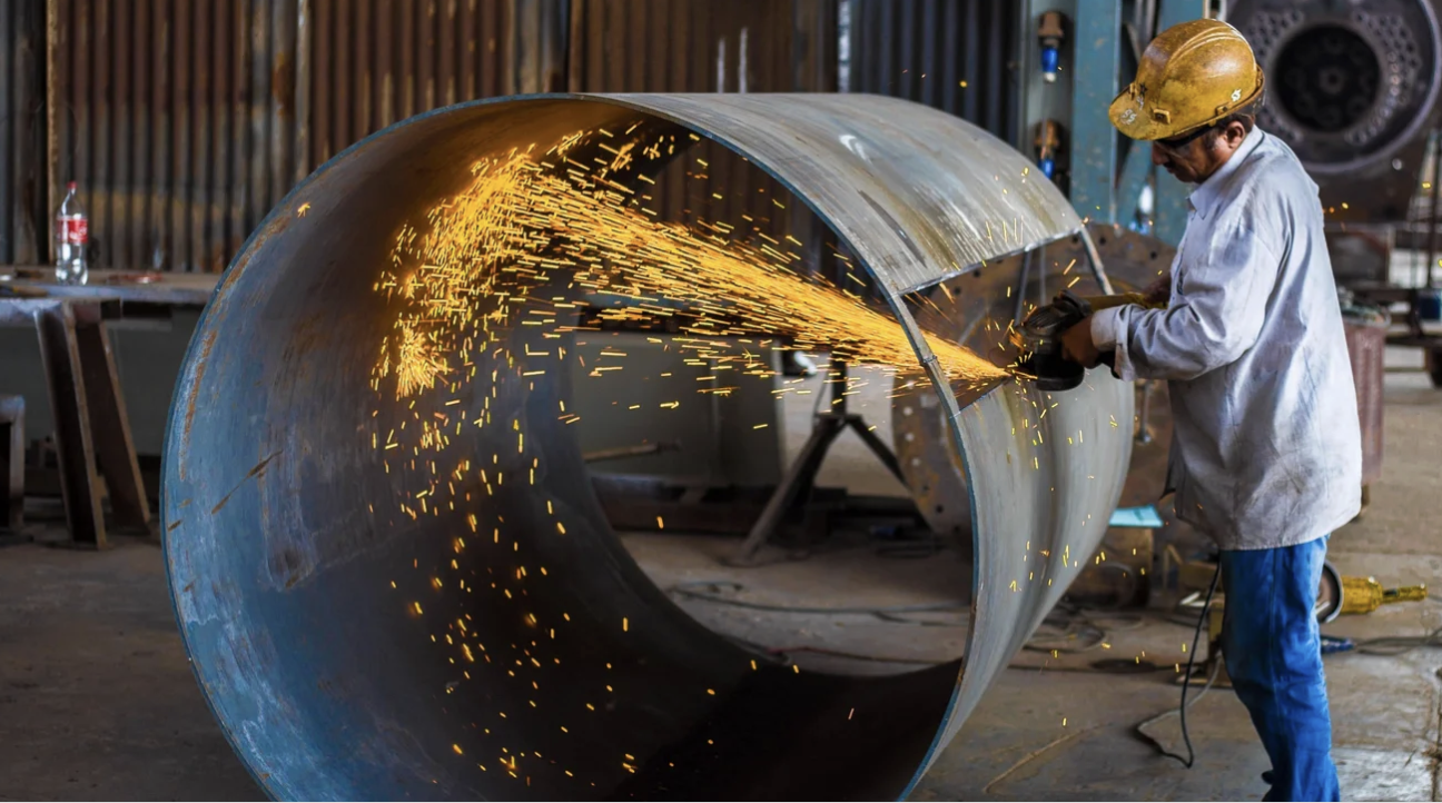 Man wearing yellow hard hard, welding a large open barrel 