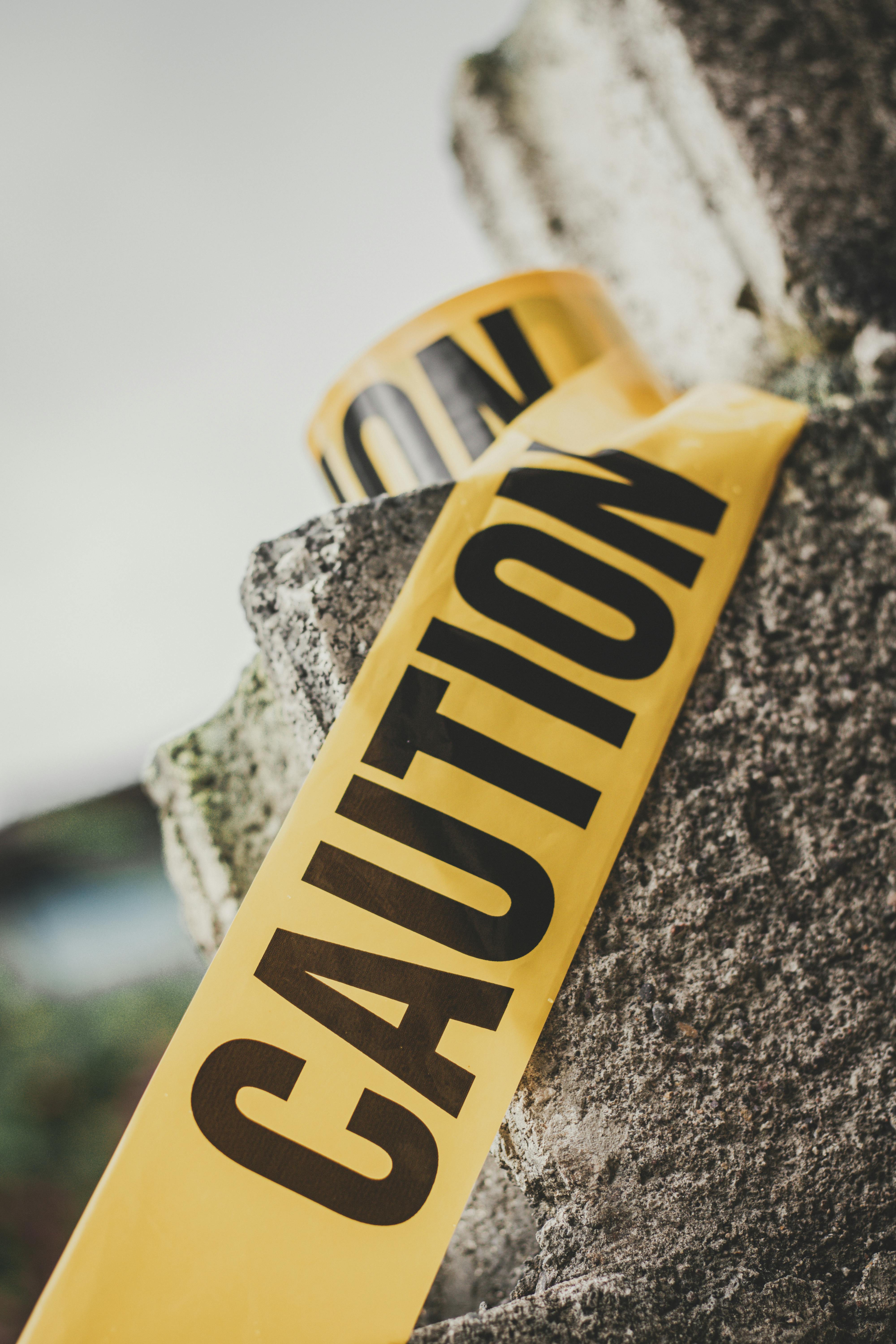 Vibrant yellow caution tape wrapped around a stone in an outdoor setting.