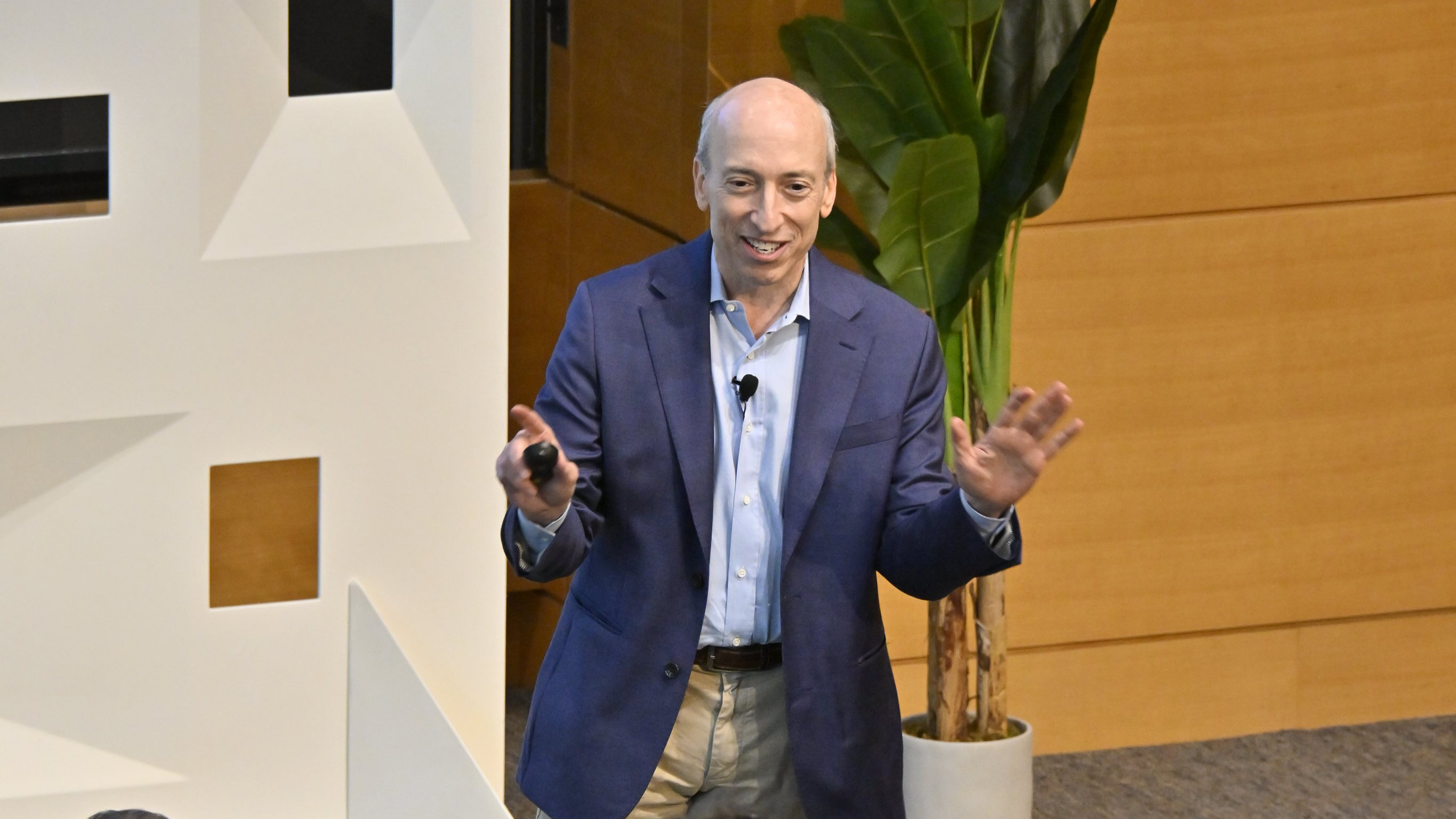 Man in business casual suit gestures before audience during presentation