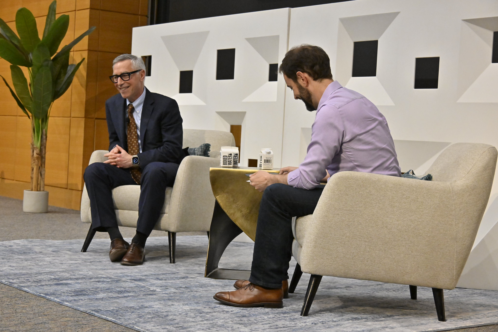 Two men laugh during a fireside chat.