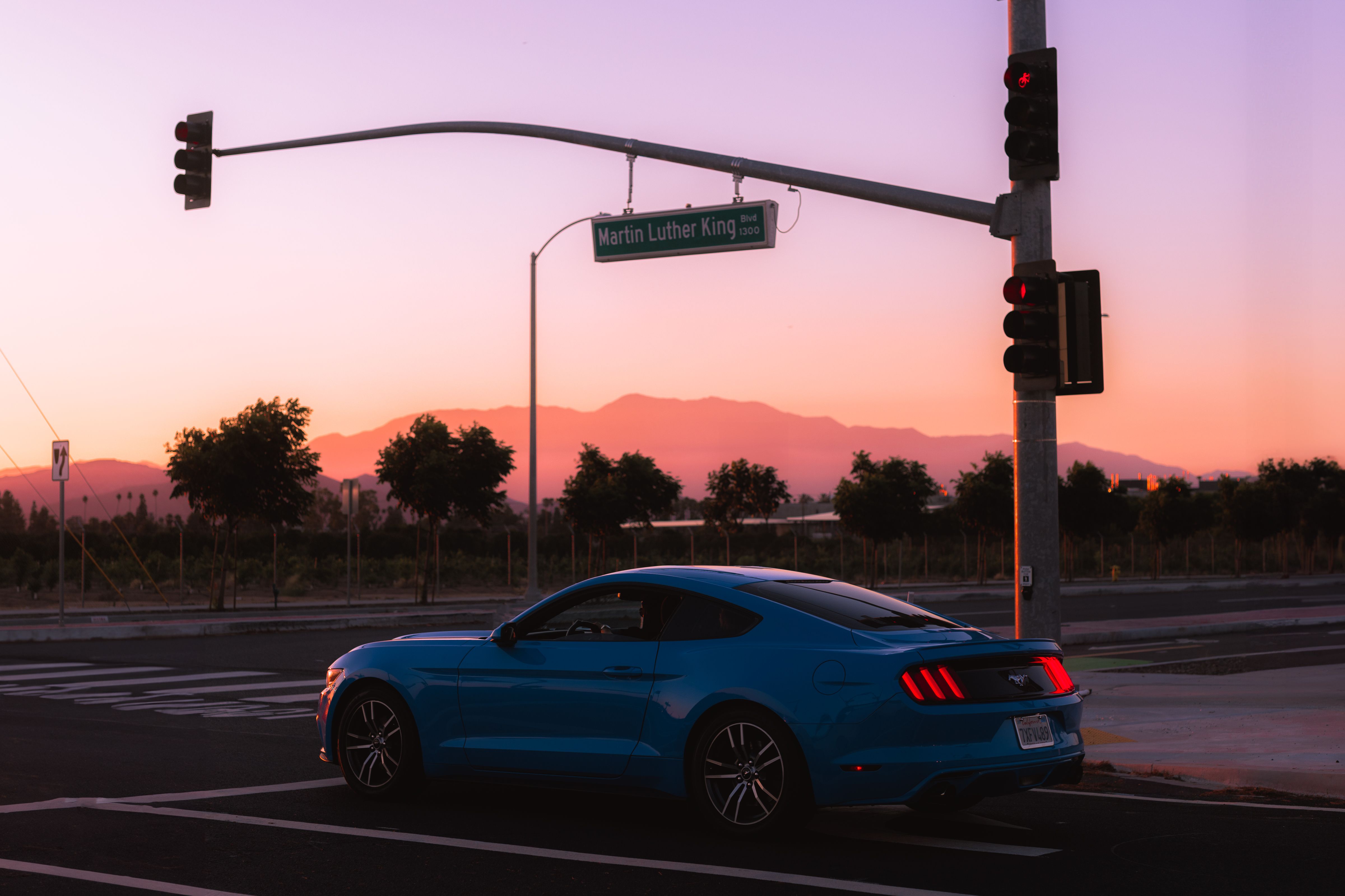 Blue sports car at a road intersection during sunset with a mountainous backdrop.