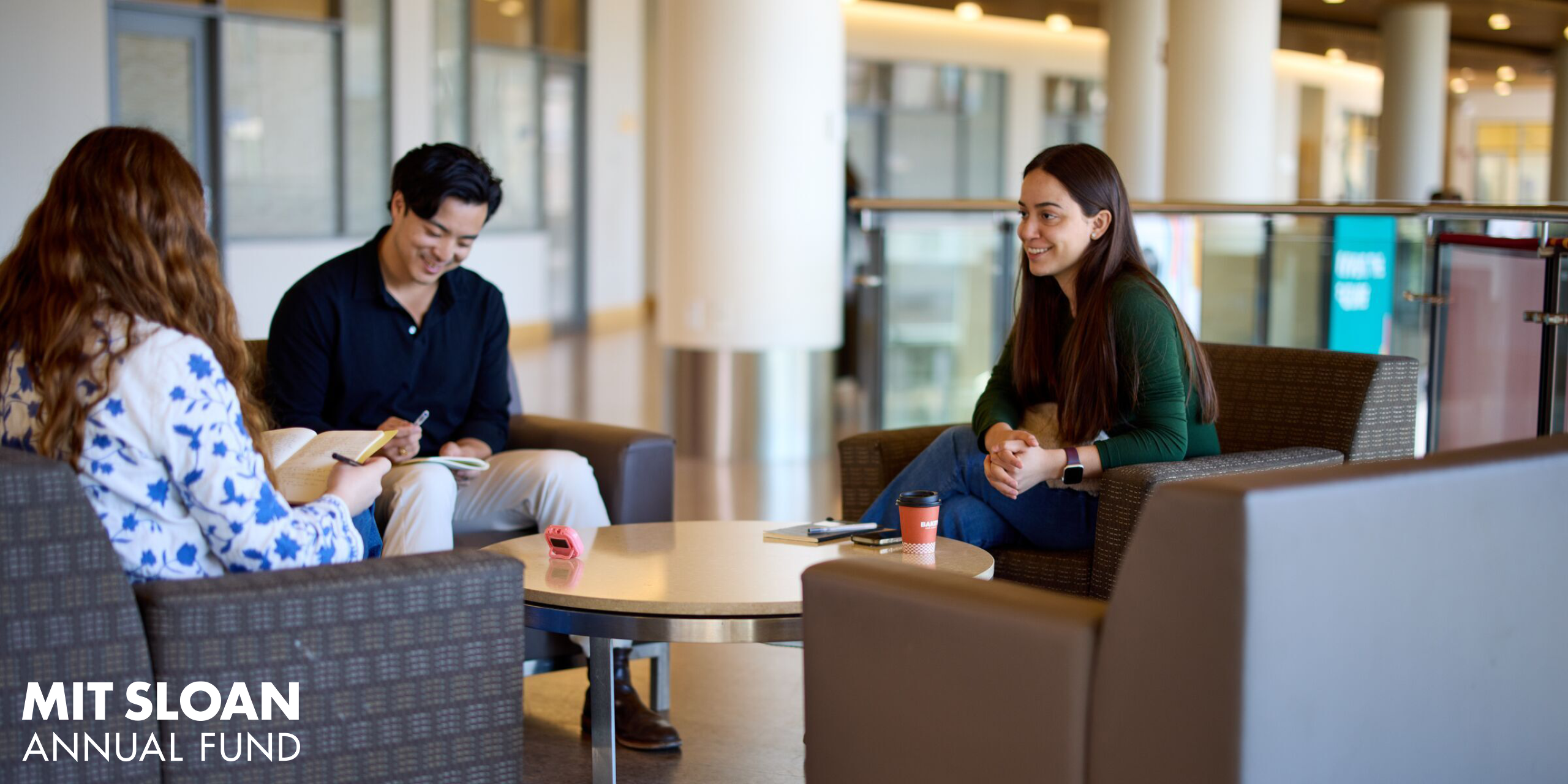 Three students converse in chairs in MIT Sloan common area