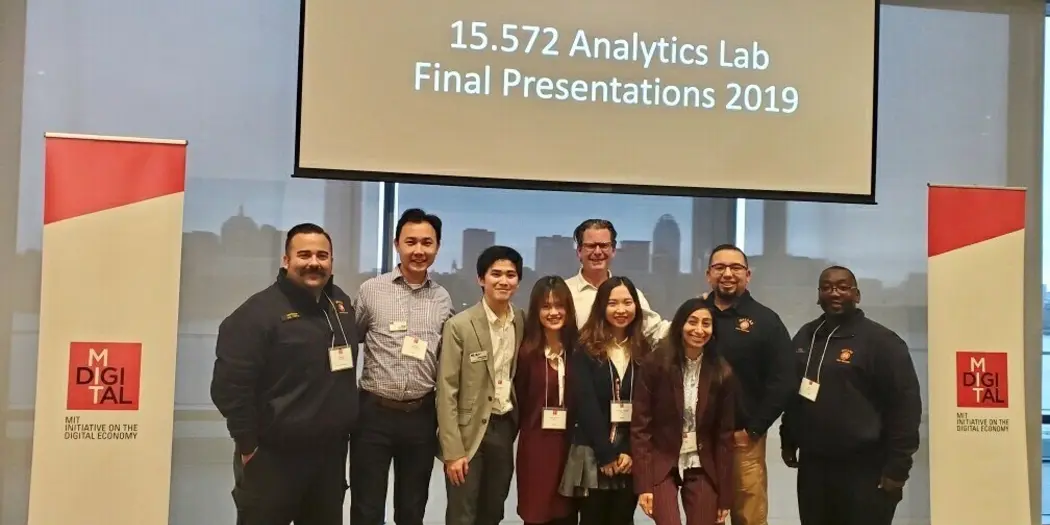 A-Lab Team and Dallas Fire and Rescue Department posing in front of presentation screen in Samberg Conference Room, MIT Sloan campus
