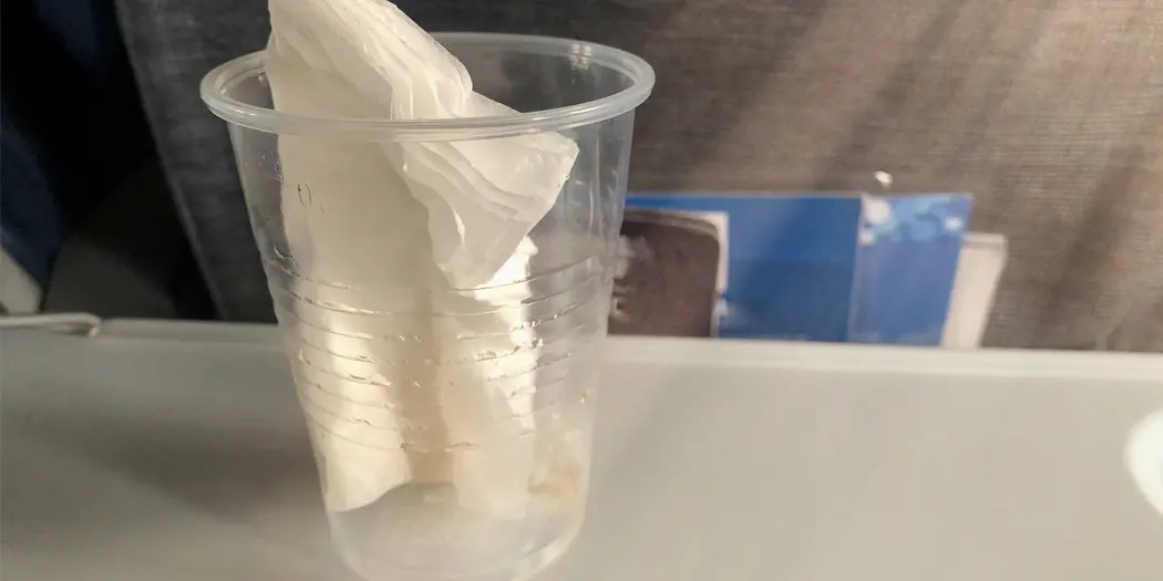 Plastic cup with paper napkin inside sitting on airplane tray table