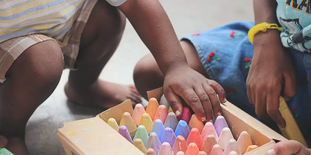 Two children kneeling over a wooden box of colorful chalk