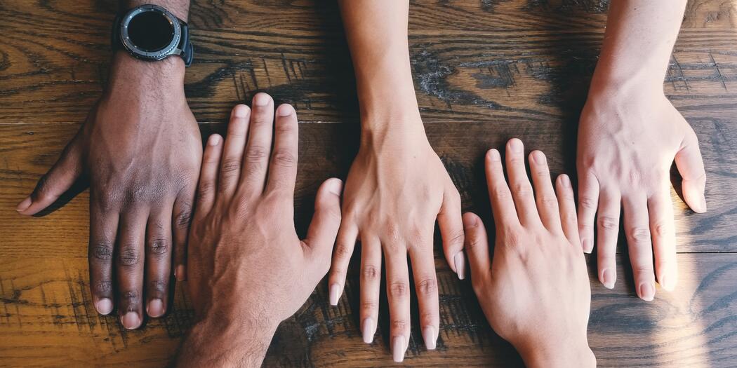 Five hands of different skin colors on a table