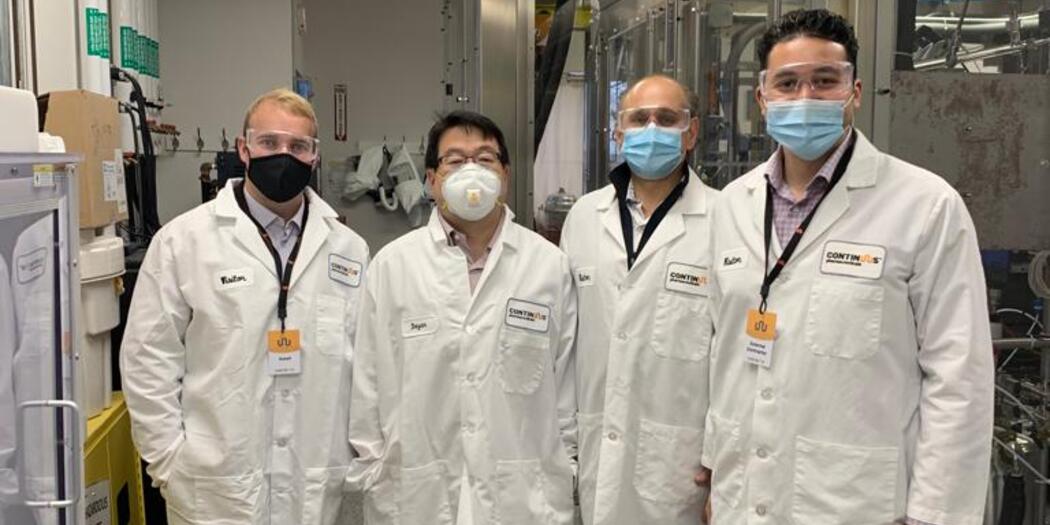 Three H-Lab students and Bayan Takizawa posing in lab coats at Continuus Pharmaceuticals