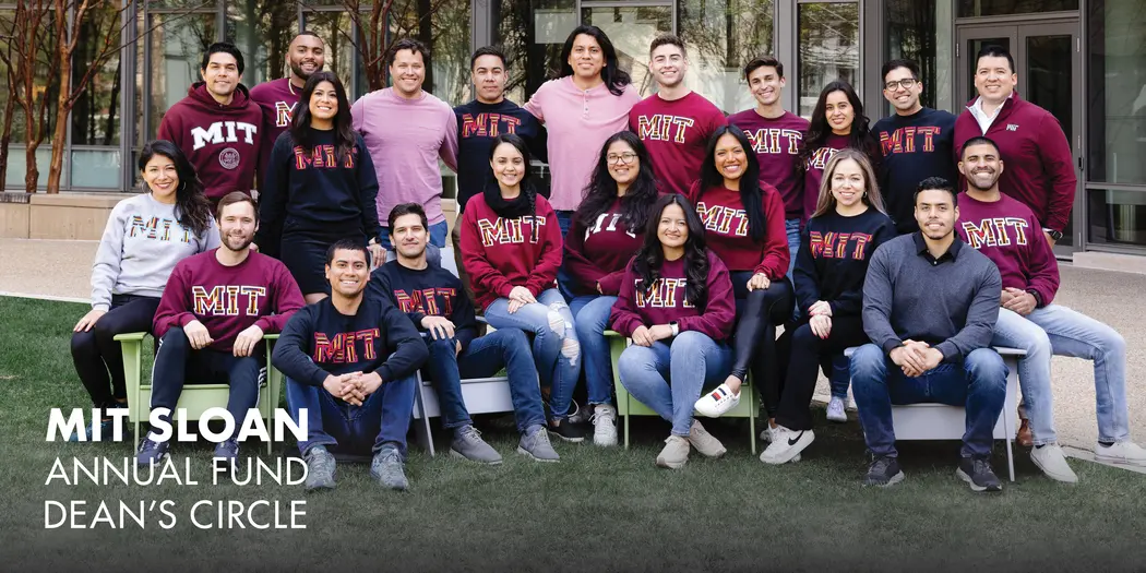A group of students wearing MIT sweatshirts pose for a photo outside of Building E62