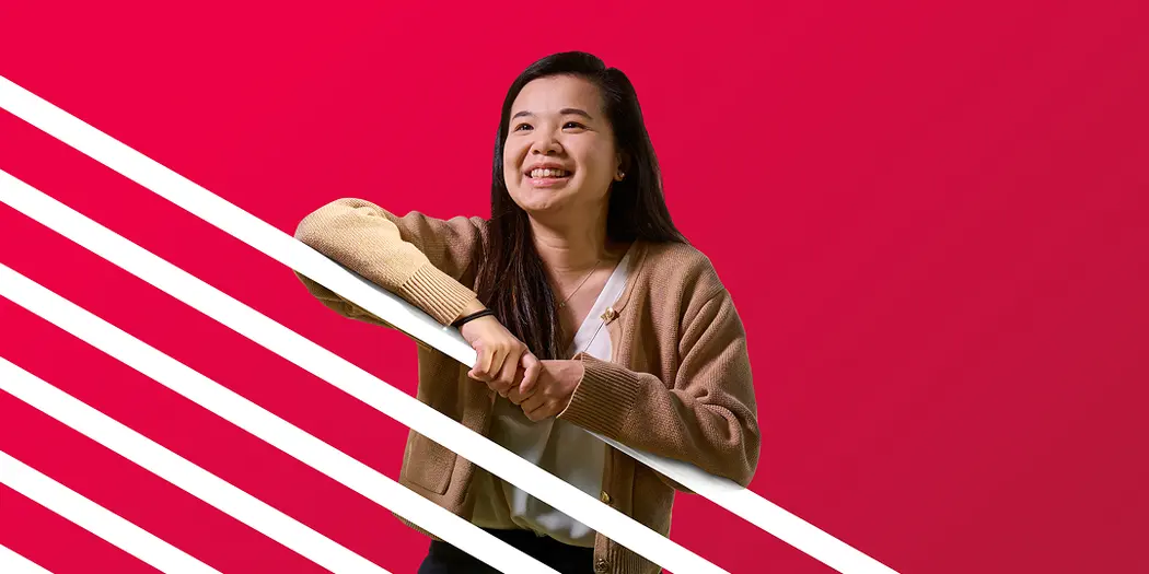 An MIT Sloan student looks off camera, smiling, with a red background with white stripes