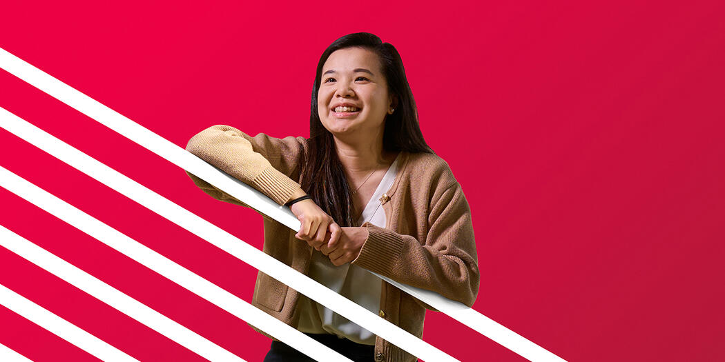 An MIT Sloan student looks off camera, smiling, with a red background with white stripes
