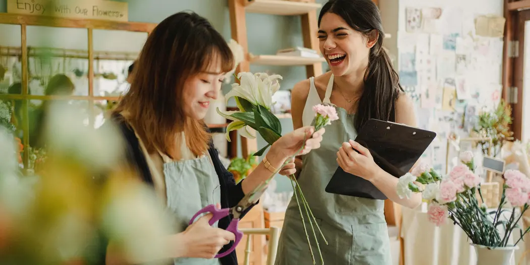 Two women who are colleagues in a florist shop, looking happy