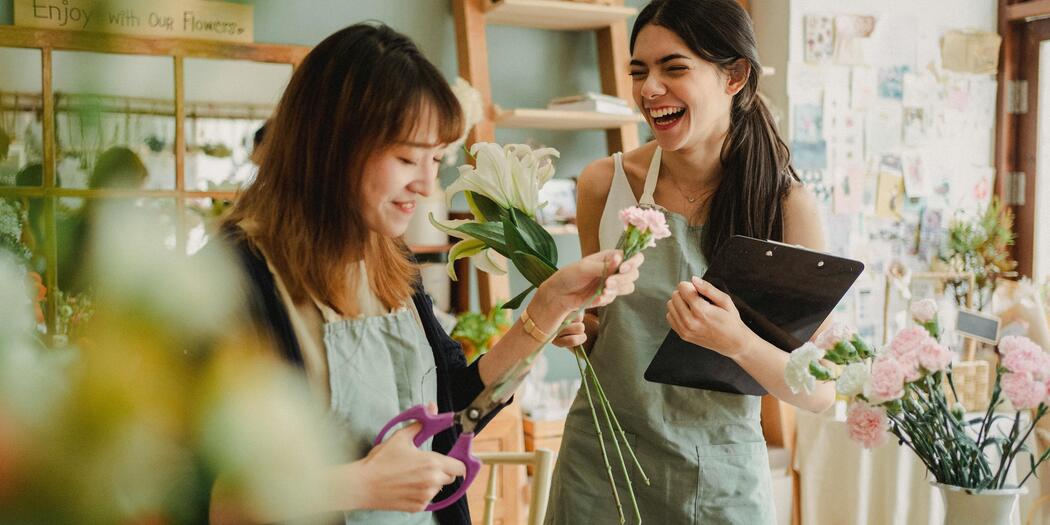 Two women who are colleagues in a florist shop, looking happy
