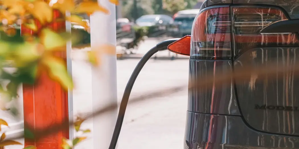 Image of the rear of an electric car being charged; the charger is visible.