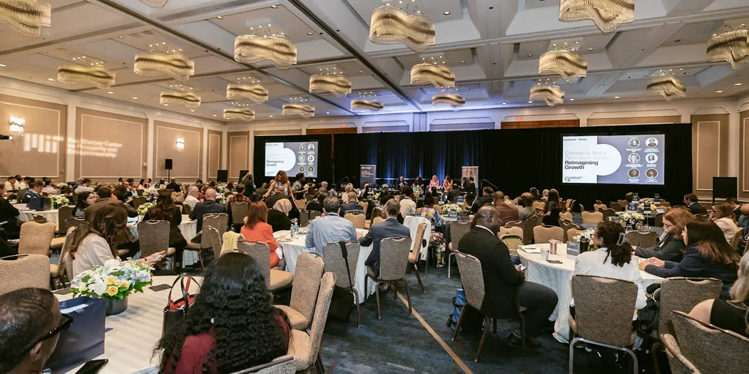 People sitting in a conference room looking up at a stage with panelists and two screens.