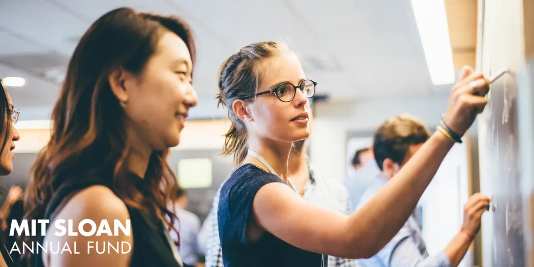 Two students solve an equation on a classroom chalkboard.