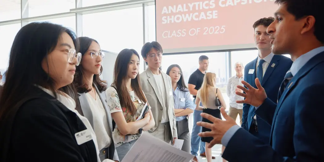 Two MBAn students present their capstone projects while four people listen. 
