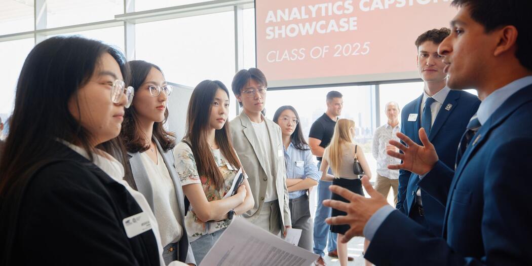 Two MBAn students present their capstone projects while four people listen. 