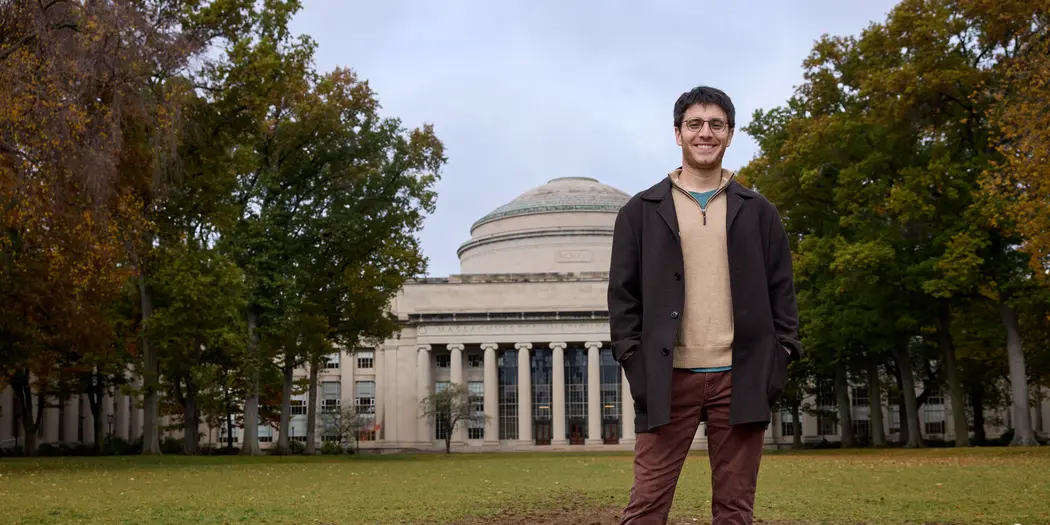 PhD student Ben Manning smiles at the camera. He stands in front of the MIT dome