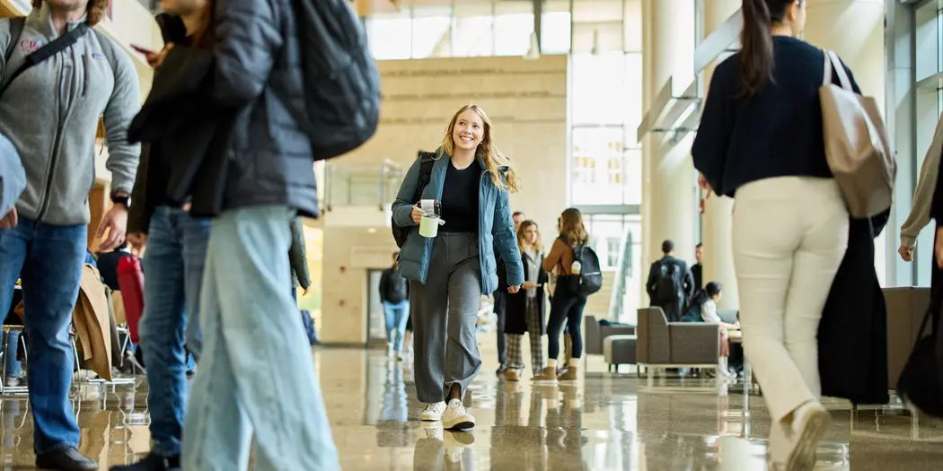 A smiling student walks through a bustling MIT Sloan common area