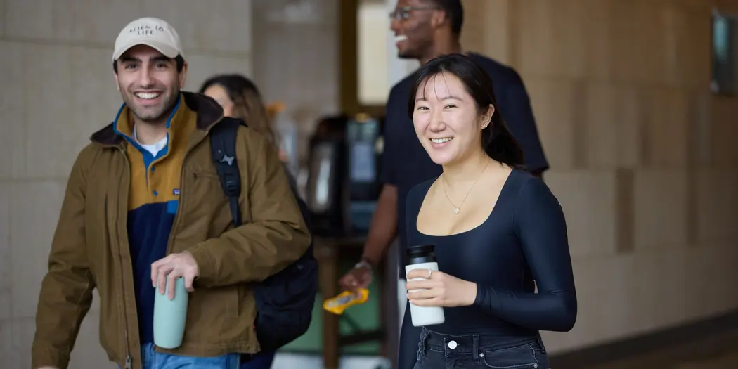 Two students smile while walking together through MIT Sloan common area
