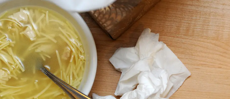 Chicken noodle soup next to tissues