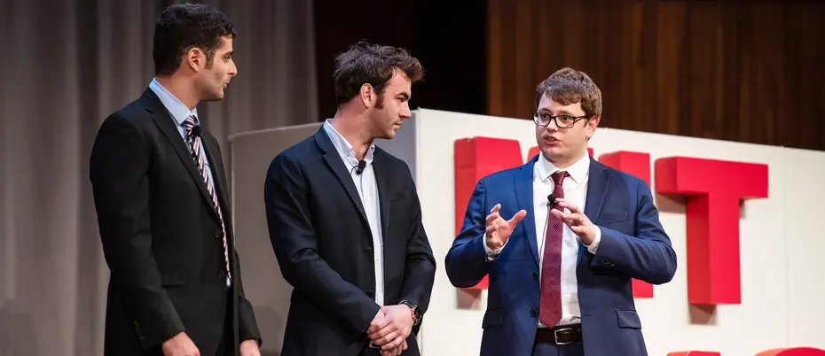 three men in suits stand on a stage