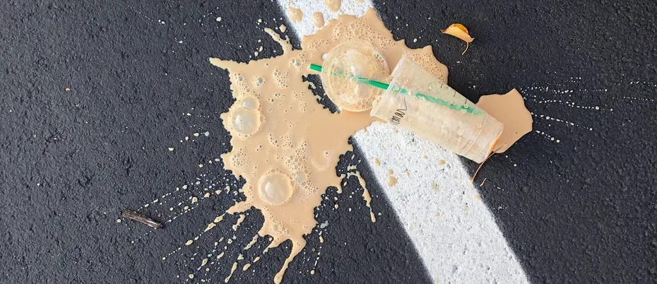 a plastic cup of coffee spilled on a black pavement