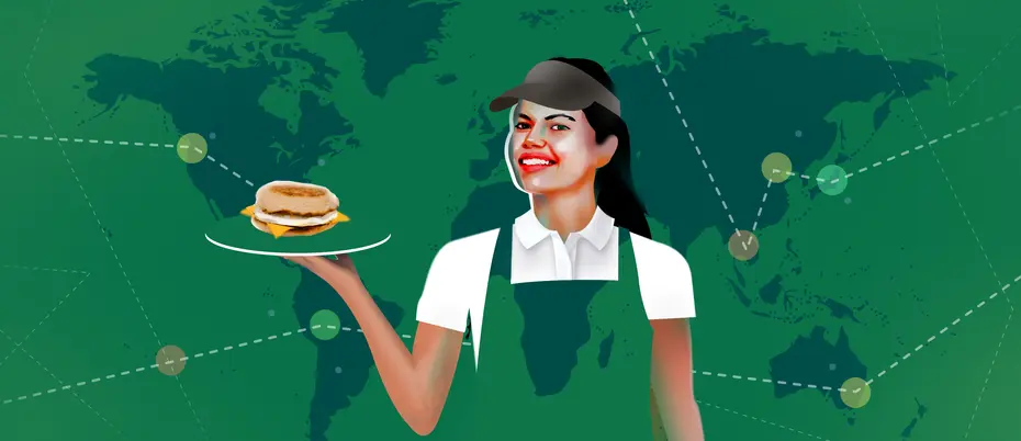 Barista in green apron holding breakfast sandwich in front of supply chain map