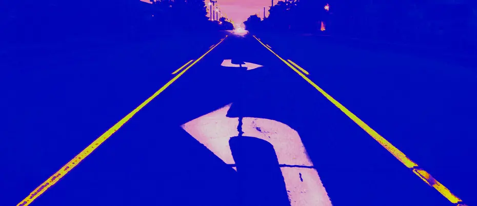 a road disappears into the horizon, with a large white turning arrow in the foreground