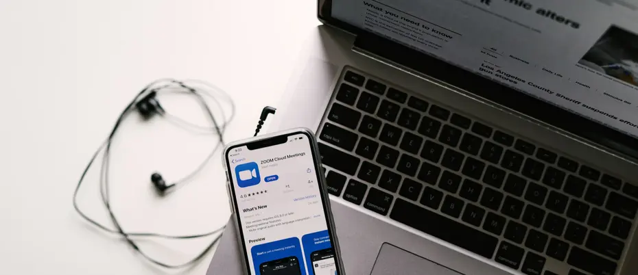 Smartphone showing Zoom app sitting next to laptop and headphones.