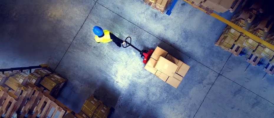 a warehouse worker pulls a wheeled pallet of boxes through a corridor