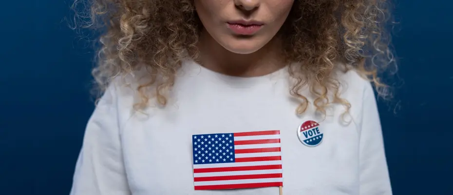 Woman frowning, wearing a "Vote" pin and holding an American flag 