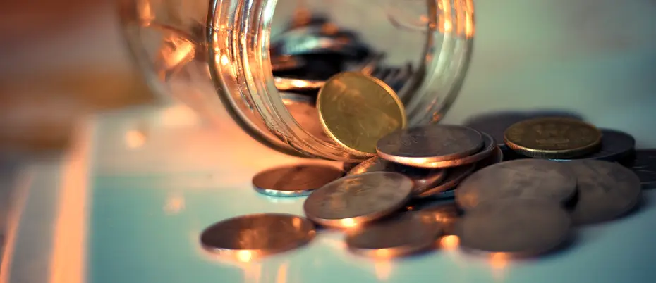 A photograph of a glass jar on a table with coins falling out