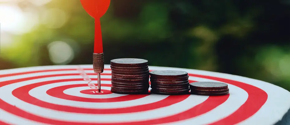 A dart arrow hitting the center of a dart board with coin stacks