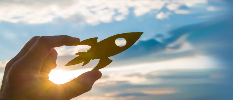 Hand holding small rocket ship against the sky.