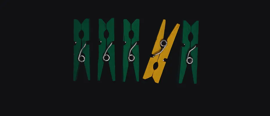 A yellow clothes pin among a row of green ones