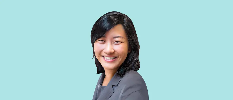 Kristin Kagetsu, co-founder of Saathi, faces the viewer and smiles. She stands in front of a light blue background and she is wearing a gray suit coat.