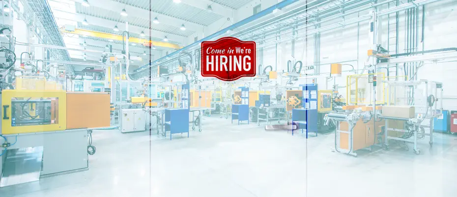 A hiring sign hangs on doors to a manufacturing plant