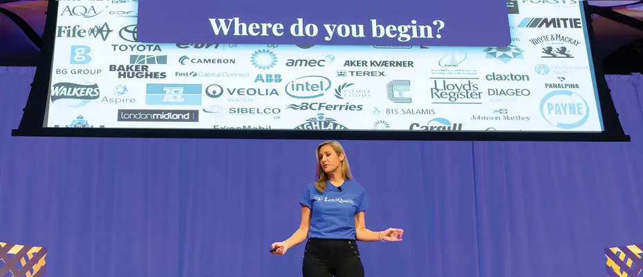 Lea Gabrielle Potts of LeadQualify at the MIT Delta V event presents on stage with the words "Where do you begin?" on screen