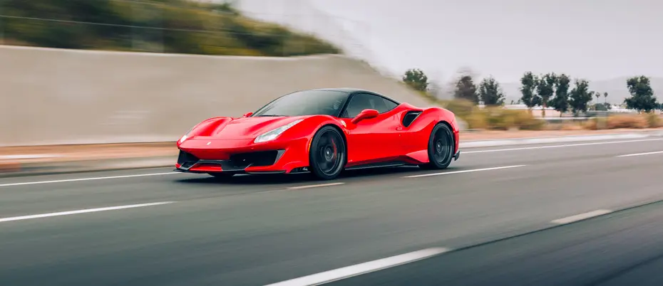 Red Ferrari on highway with blurred trees and coastal scene in background