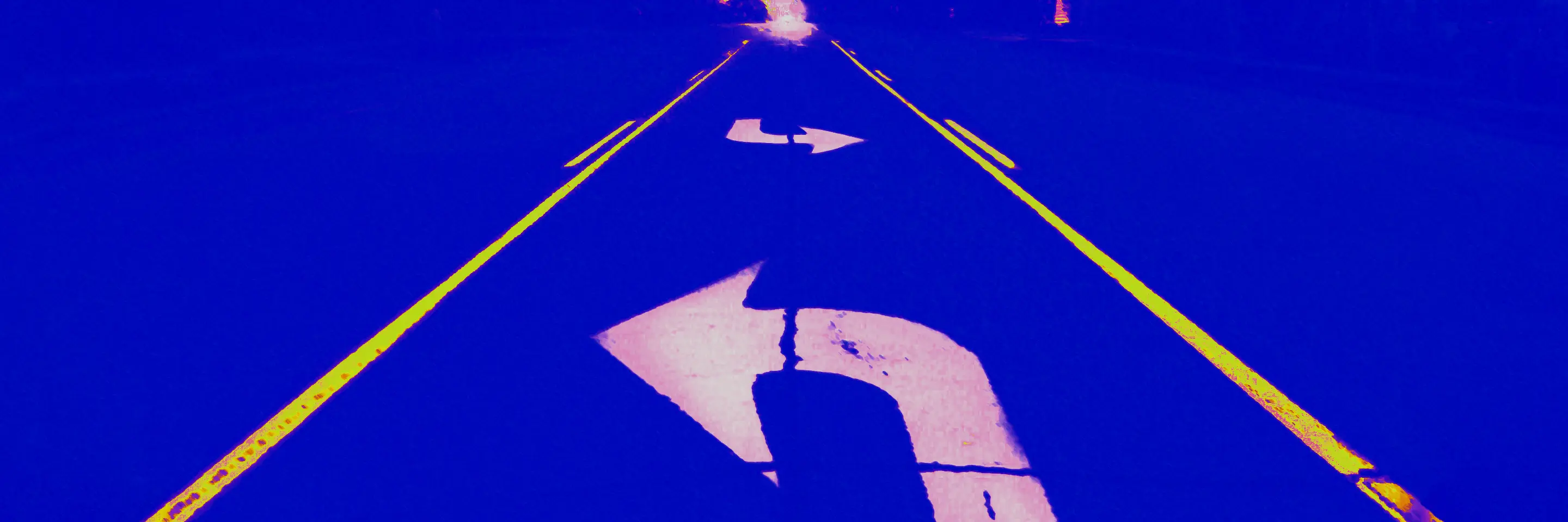 a road disappears into the horizon, with a large white turning arrow in the foreground