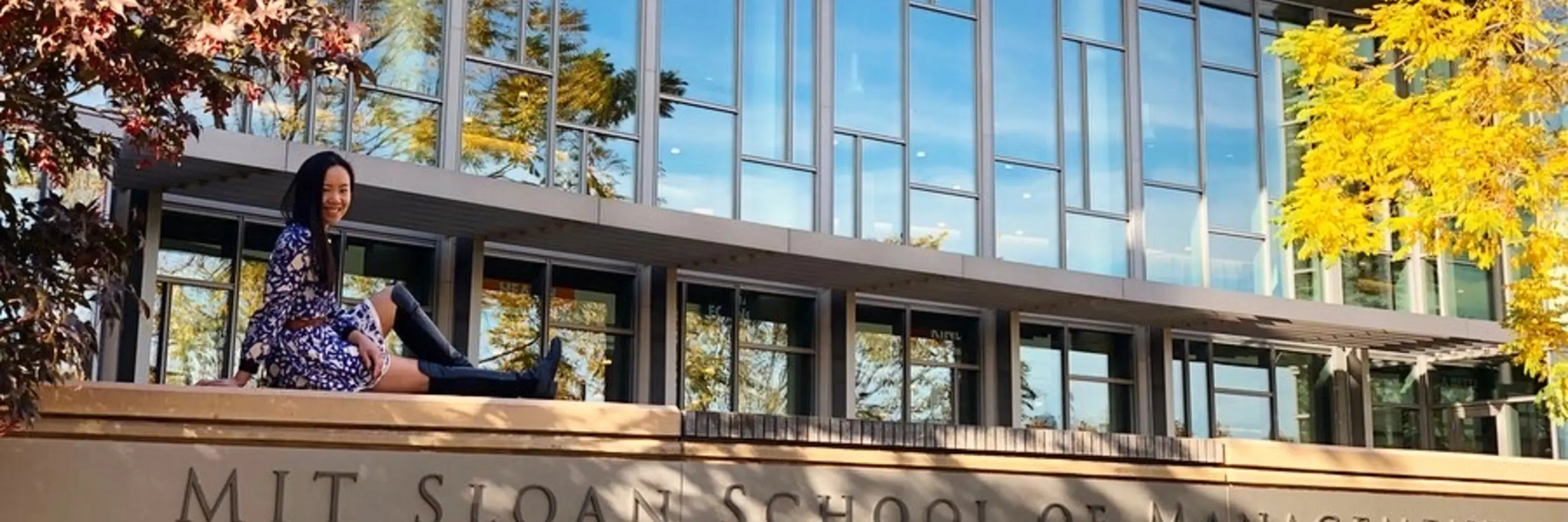 Ivy Wang, MBA 2021 sitting at the MIT Sloan sign in front of E62