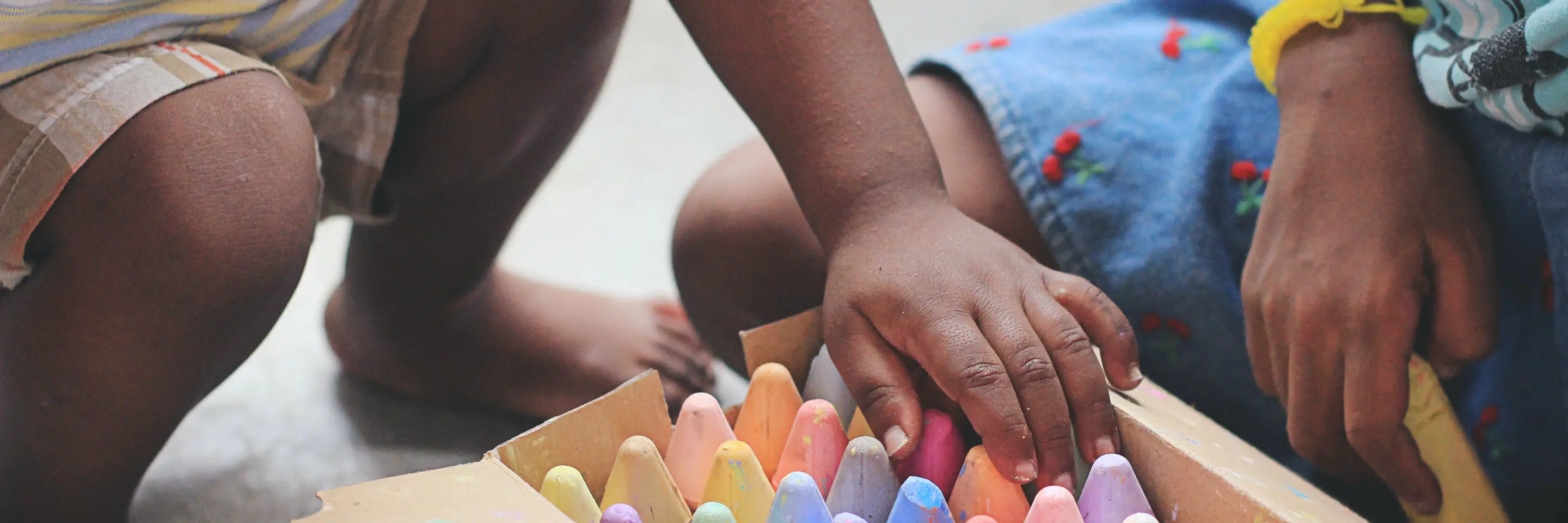 Two children kneeling over a wooden box of colorful chalk