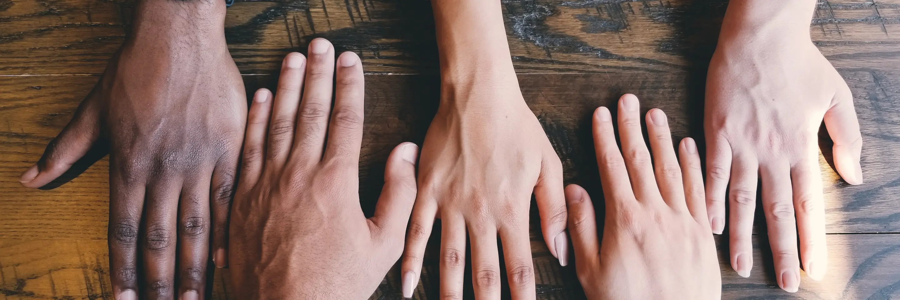 Five hands of different skin colors on a table 