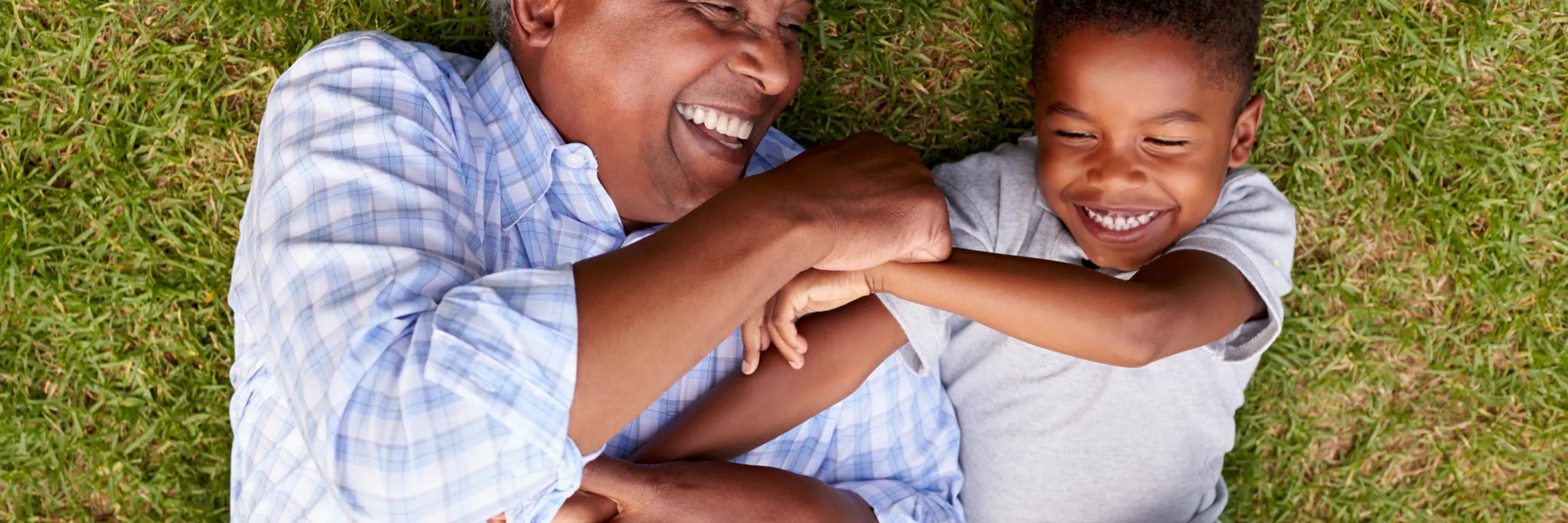 Grandfather and grandson play lying on grass, aerial view