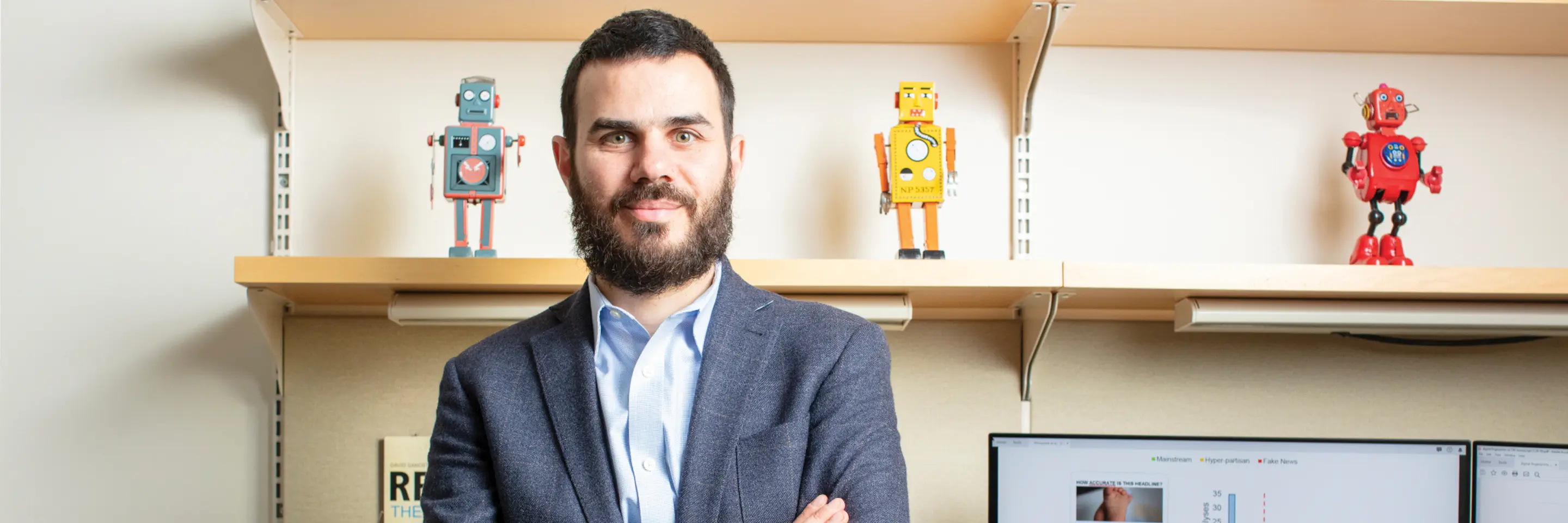 David Rand stands in front of shelves with three small robots on display