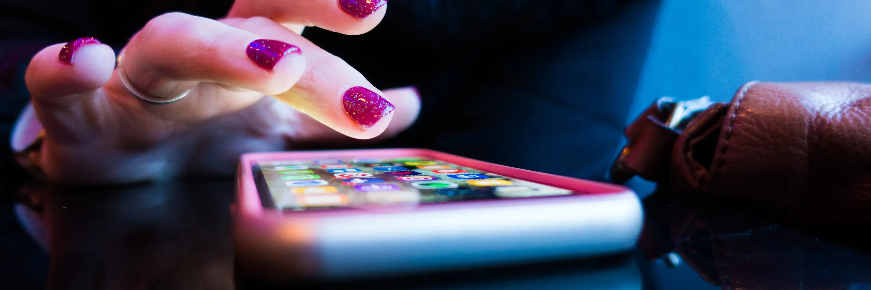 Hand with pink nail polish hovering over cell phone on table